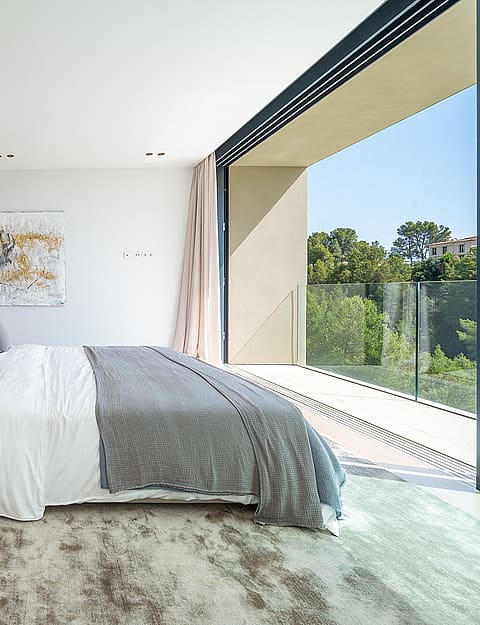 A modern bedroom featuring a bed placed against a dark partition, with floor-to-ceiling glass doors opening to a terrace.