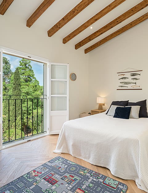 Bright bedroom featuring slanted timber ceiling beams, herringbone oak floors, and glass doors opening to a garden view.
