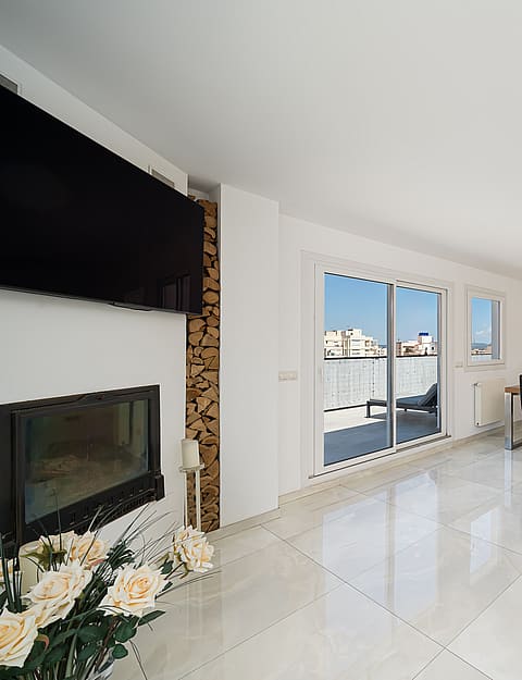 Bright open-plan living room with white marble floors, a recessed fireplace, and a dining set leading to a terrace.