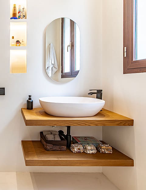 Modern bathroom featuring a floating double-tier oak vanity, white vessel sink, and an oval wall mirror against light walls.