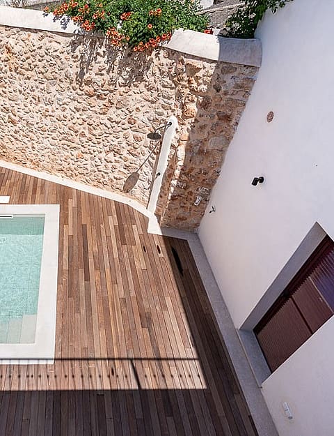 High-angle view of a small rectangular plunge pool surrounded by a wooden deck and high white walls with a natural stone feature wall.
