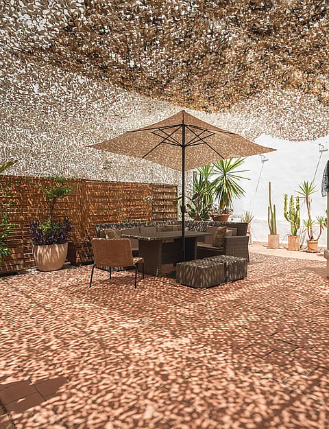 Outdoor terrace with camouflage netting shade, dining table, and a daybed on a terracotta tiled floor.