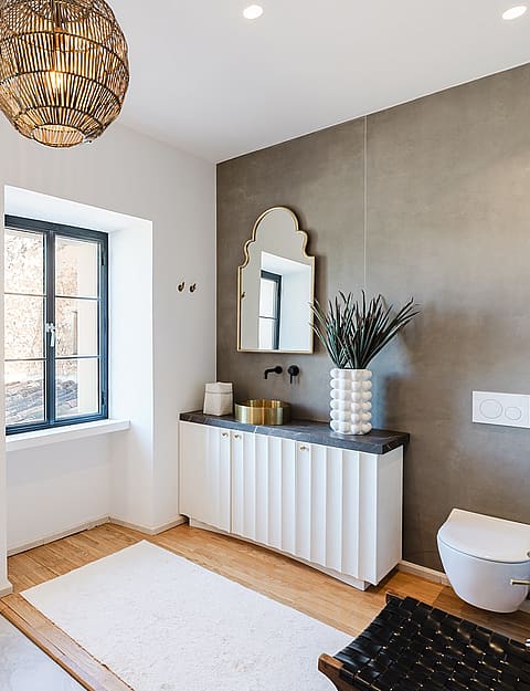 Bathroom with white fluted vanity, gray accent wall, arched mirror, and warm pendant lighting.