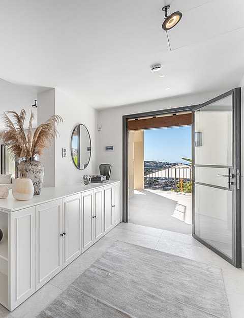 Sunlit hallway featuring white built-in storage and an open glass door leading to a terrace with distant views.