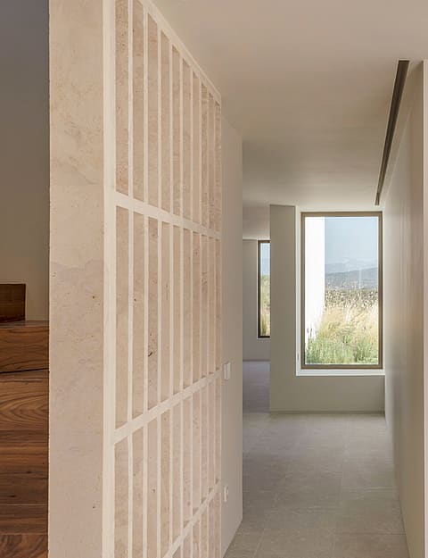 Minimalist hallway with a decorative stone partition and large windows viewing a Mediterranean garden.