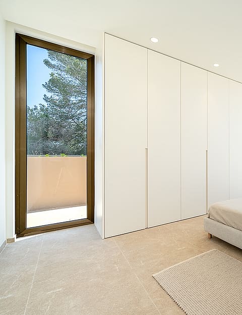 Modern bedroom with a large white floor-to-ceiling built-in wardrobe, a neutral bed, and sliding glass doors opening to a terrace.