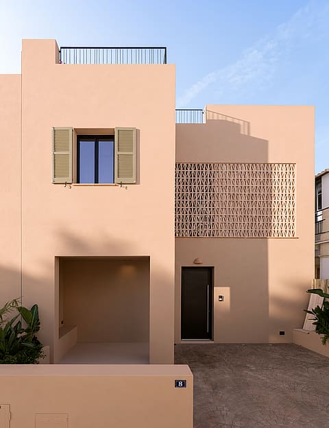 Front view of a two-story beige townhouse in Genova with geometric terracotta latticework and a covered entrance alcove.