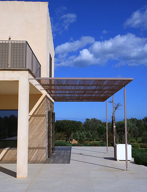 Exterior terrace of a Mallorcan finca with a metal laser-cut pergola casting intricate shadows on the stone floor.
