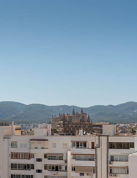 Panoramic view of a coastal city with white buildings and distant mountains under a clear blue sky.