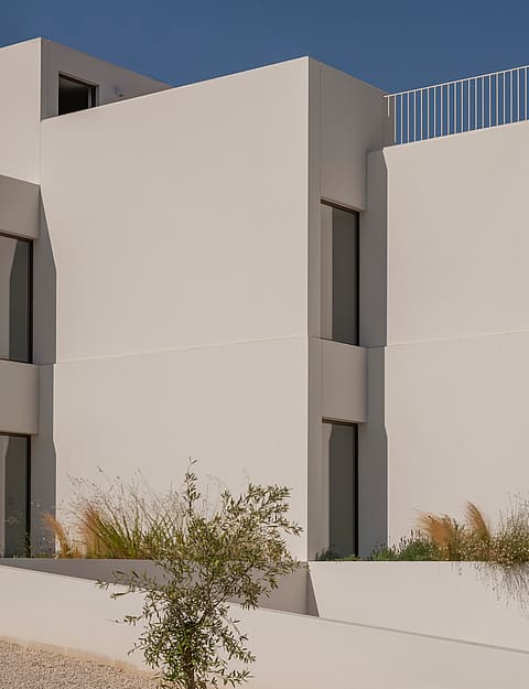 Modern white geometric building exterior featuring sharp vertical lines, small windows, and native grasses in the foreground.