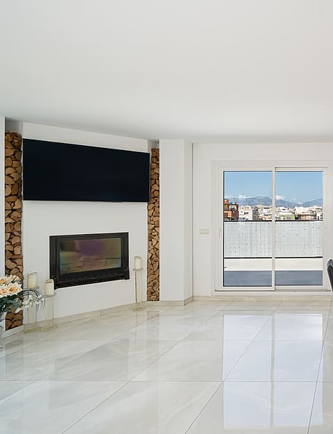 Dining room with a wooden table, black chairs, and a fireplace with a mounted television, featuring city views through glass doors.
