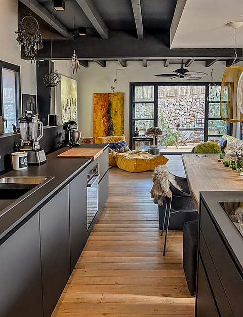 Contemporary kitchen with matte black cabinetry and wooden floors leading to an outdoor terrace with stone wall views.
