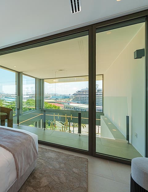 Dormitorio moderno con cama grande, decoración neutra y ventanales correderos con salida a la terraza.