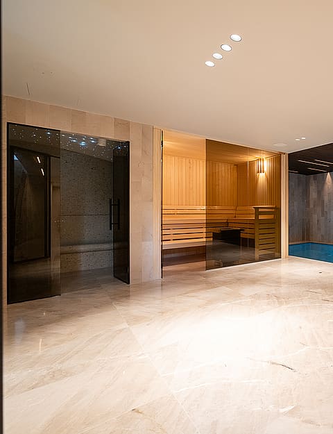 Indoor spa area featuring a tiled lap pool, sauna with glass door, polished stone flooring, and recessed ceiling lighting.