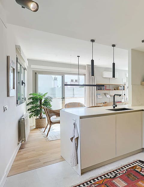 A contemporary white kitchen featuring a peninsula island, track lighting, and a patterned rug on the floor.