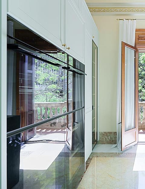 Modern kitchen featuring a dark stone island, sleek white cabinetry, and French doors opening to a stone-railed balcony.