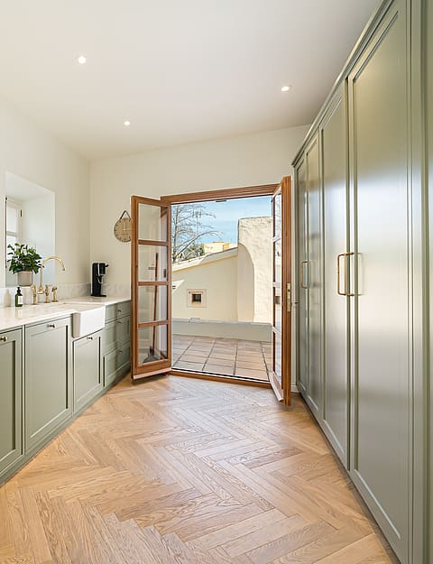 Contemporary kitchen featuring sage green shaker cabinets, white stone countertops, and light oak herringbone floors.