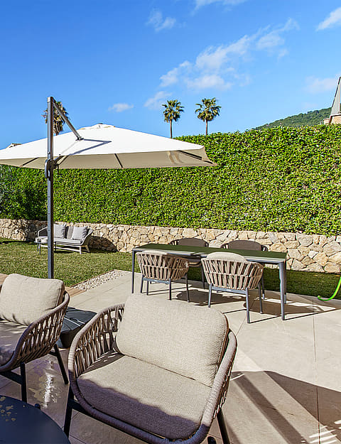 A backyard garden with a small swimming pool, wooden decking, a dining set under an umbrella, and woven outdoor lounge chairs.