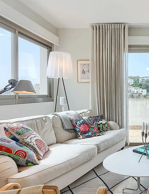 A bright living room with a beige sofa, patterned pillows, round coffee table, and large glass doors opening to a terrace.