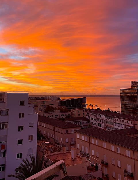 A high-angle view over an urban cityscape and water during a vivid orange and purple sunset.