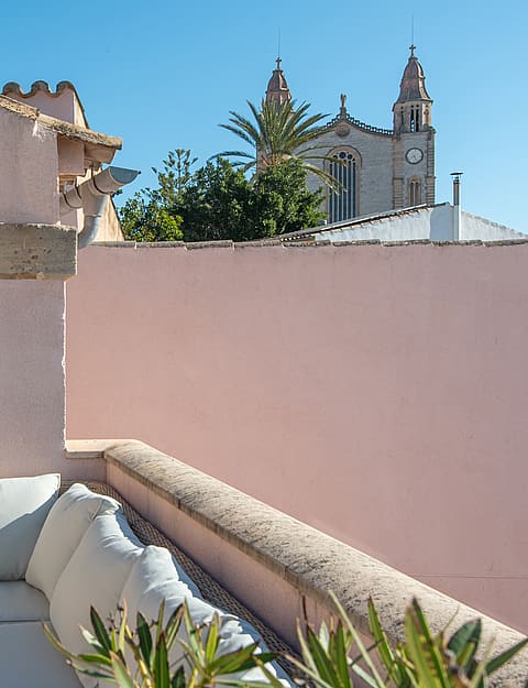 Outdoor terrace featuring exterior sofas, soft pink walls, and views towards the church tower in Calvià.