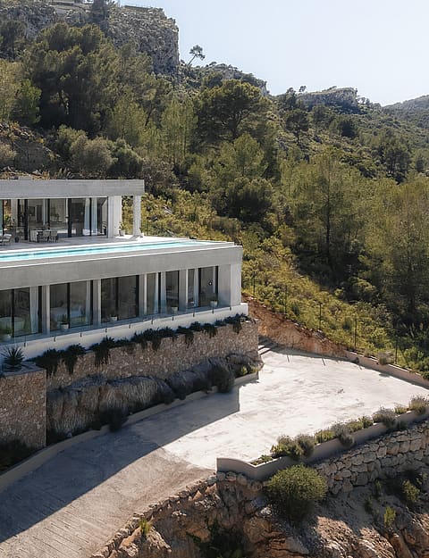 Aerial perspective of a multi-level modern villa featuring an infinity pool, stone walls, and glass facades in Son Vida.