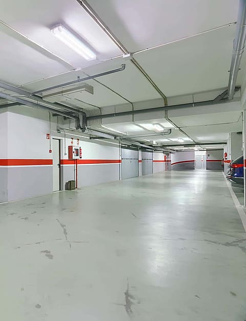 A clean, well-lit underground parking garage with white and grey walls, red accent stripes, and marked parking spaces.