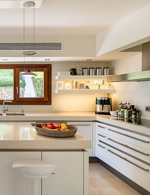 Fully fitted kitchen with white cabinetry, stone worktops, central island, Miele ovens and garden window