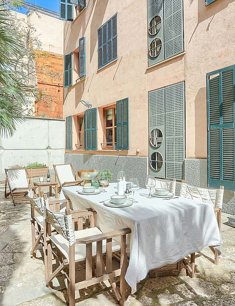 Outdoor terrace in a historic Old Town building with a dining table, folding wooden chairs, and green shutters.