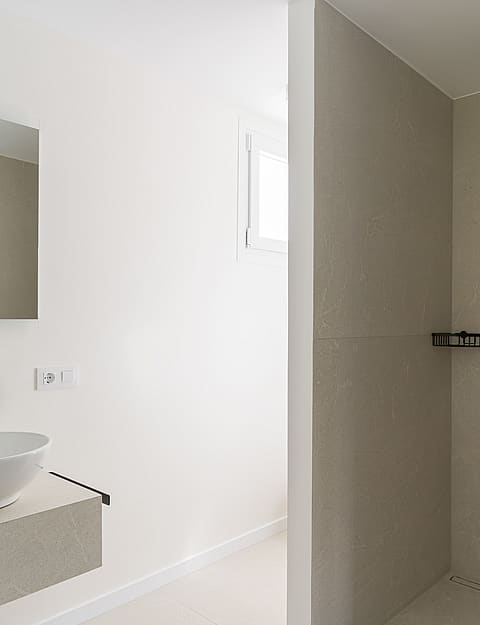 Modern walk-in shower featuring large-format sand-colored tiles and contrasting matte black rain shower and handheld spray.