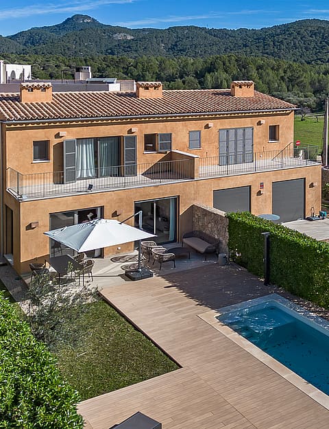 Aerial view of a Mediterranean townhouse with a terracotta roof, private pool, and landscaped garden against a mountain backdrop.