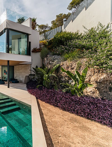 Modern two-story villa with glass walls and stone terracing, set against a rocky hill with an infinity-edge swimming pool.