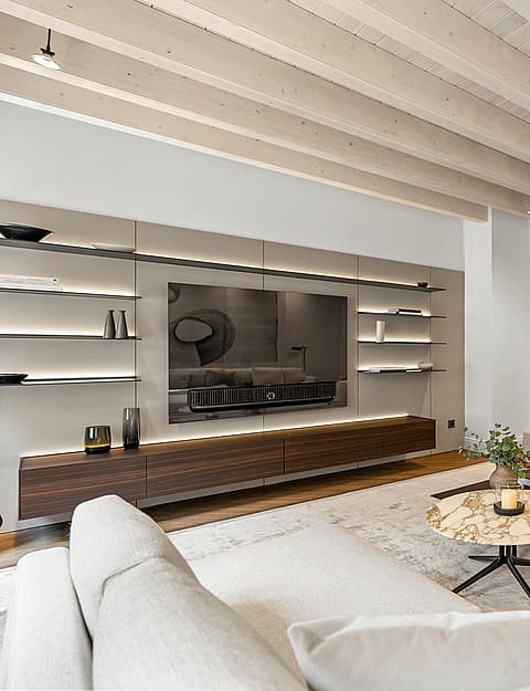 Contemporary living room featuring whitewashed ceiling beams, integrated backlit shelving, and a marble coffee table.
