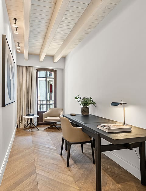 Minimalist home office featuring chevron wood flooring, exposed timber beams, a dark desk, and an arched glass door.