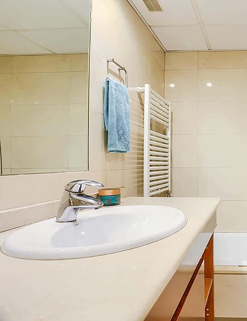 Bathroom interior featuring a white vanity with oval basin, wall mirror, towel rack, and a bathtub with a tiled enclosure.