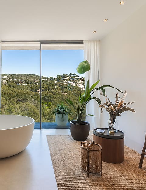 A white freestanding bathtub positioned beside floor-to-ceiling windows with views of the Son Vida landscape.