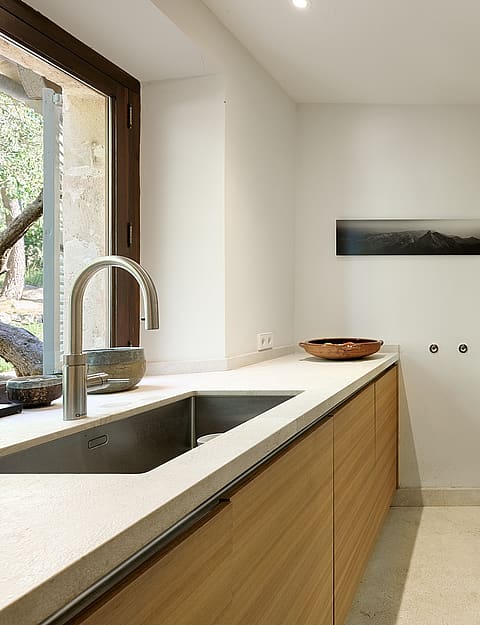 Modern kitchen interior featuring horizontal grain oak cabinets, light stone countertops, and a stainless steel sink.