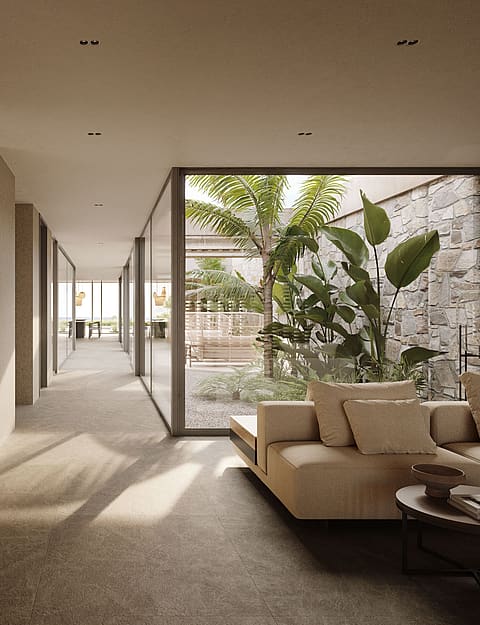 A long interior hallway with textured stone walls, modern sofa, and floor-to-ceiling glass windows overlooking a patio.