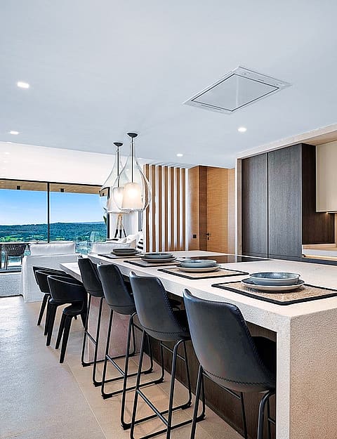 Modern kitchen with large white stone island, dark bar stools, and sliding glass doors opening to a mountain terrace.