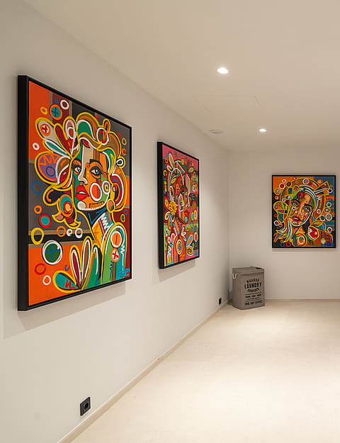 A bright, clean laundry room with white cabinetry, integrated appliances, and three vibrant abstract paintings on the wall.