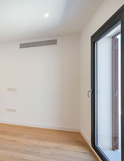 Empty bedroom interior with light wood flooring, white walls, two wooden doors, and a glass terrace door.
