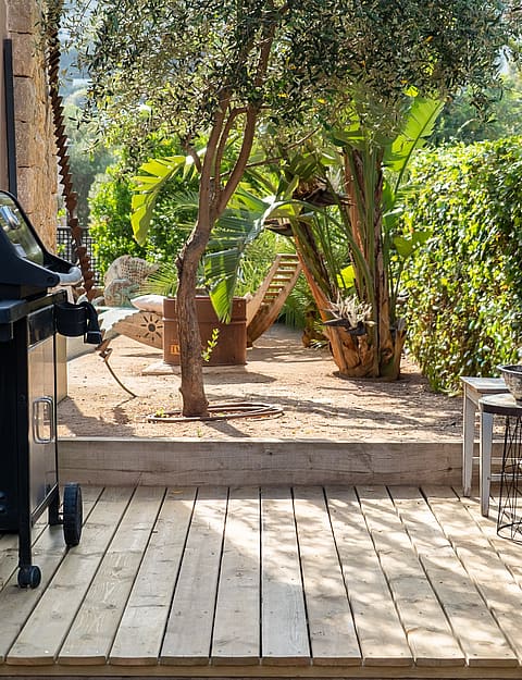 A wooden deck terrace with a barbecue grill and white rustic chairs, overlooking a garden area in Genova.