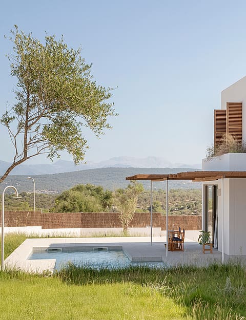 Modern white house featuring wooden shutters and a swimming pool with views of the distant mountains and green landscape.
