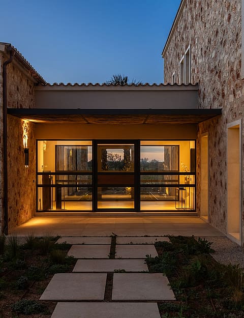 The entrance to a traditional stone finca at twilight with a stone pathway leading to a glass-paneled front door.