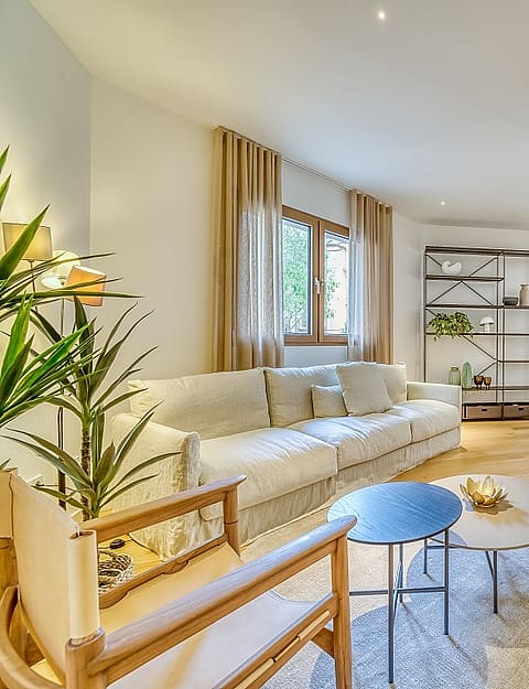 Bright open-plan living room with a beige sofa, round coffee tables, wooden flooring, and adjacent dining and kitchen areas.