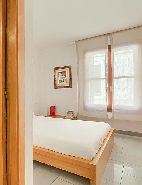 A view through a wooden doorframe showing a bedroom with a bed to the right and a bathroom vanity unit to the left.