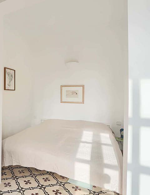Compact bedroom featuring white walls, a built-in white wardrobe, and decorative patterned floor tiles under a double bed.