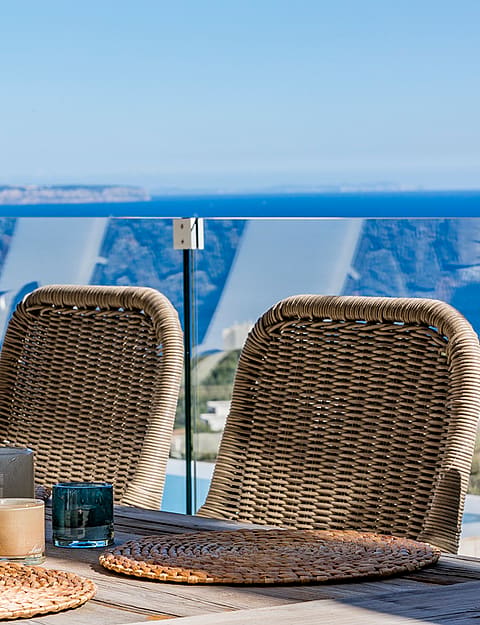 Närbild på en utomhusmatplats med korgstolar, bordstabletter och glas på en terrass med havsutsikt.