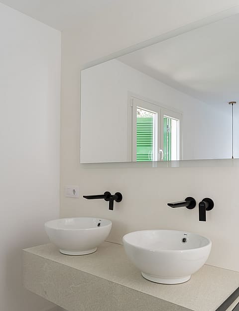 Dual white ceramic vessel sinks on a floating stone vanity with matte black wall-mounted faucets and integrated side rails.