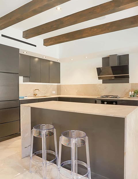 Modern kitchen with dark grey cabinetry, central stone island, and exposed timber ceiling beams in an Old Town townhouse.
